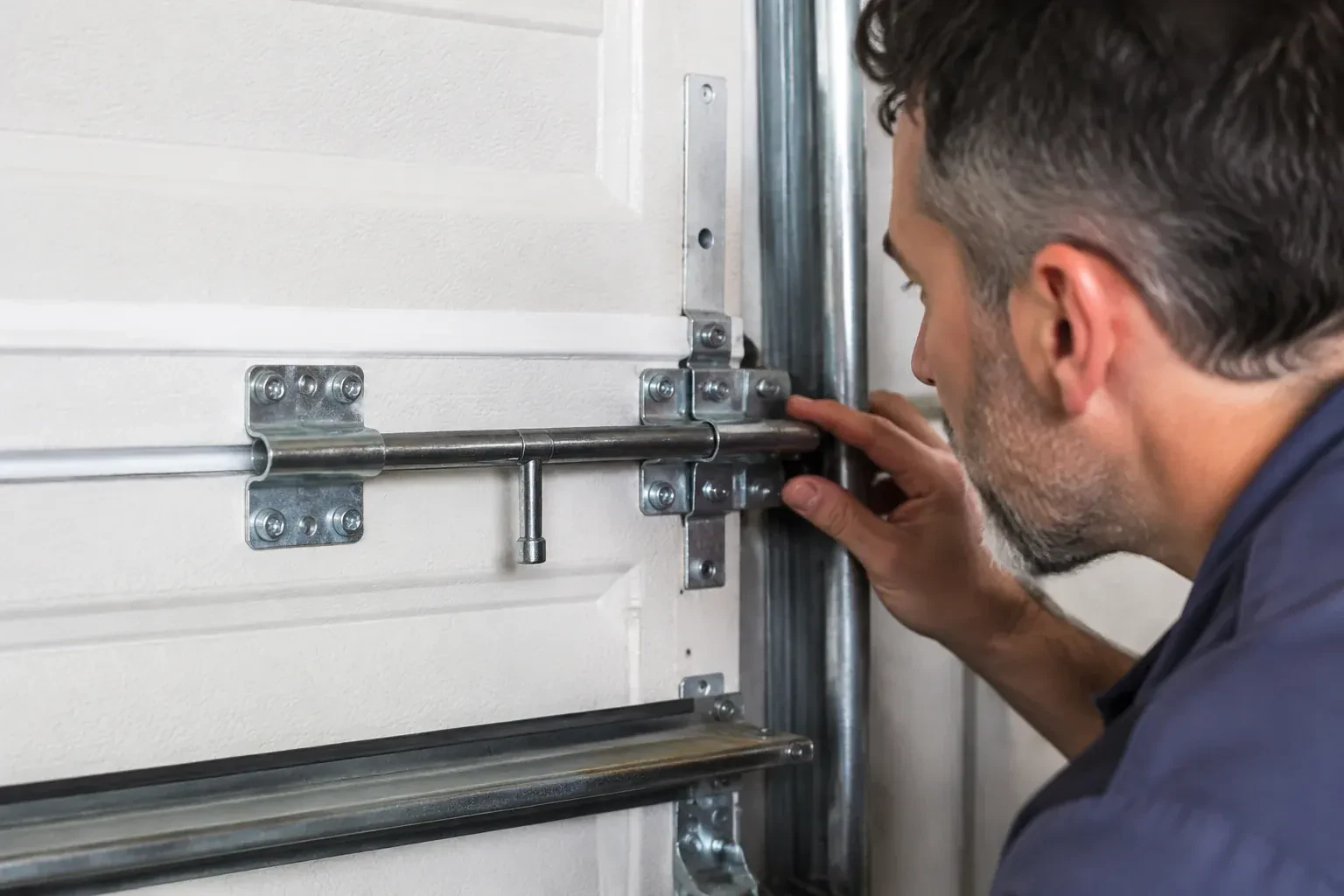 Person leaning close to a white paneled door, one hand on a metal slide-bolt bar mounted across the panel. — Garage Door Manual Lock Repair, Oshawa